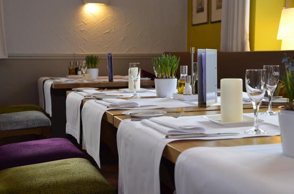 Ein gemütliches Restaurant, elegant gedeckte Tische; weiße Tischdecken, Dekoration mit Pflanzen.